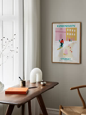 Gerahmtes Kopenhagen-Poster über einem Holztisch am Fenster in einem hellen Raum.