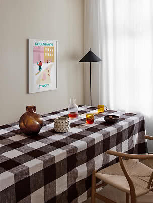Esstisch mit braun karierter Tischdecke, Gläsern und Vase in hellem Raum mit schwarzer Stehlampe
