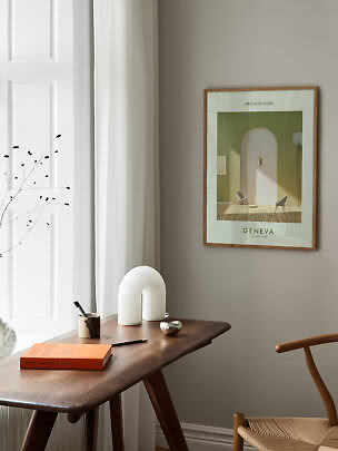 Framed architecture poster on a beige wall above a wooden desk beside white curtains