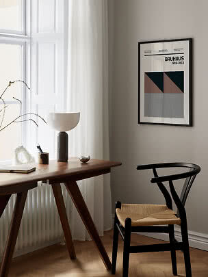 Inramad Bauhaus-affisch över ett träskrivbord vid fönstret med svart stol