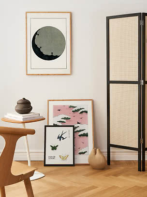 Stylish corner with framed art prints, vase on side table, and black woven room divider.