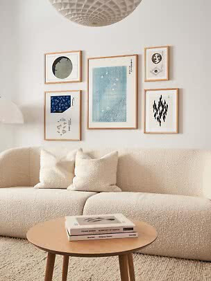 Minimalistisk stue med cremefarvet sofa, træbord og gallerivæg med fem indrammede kunsttryk.