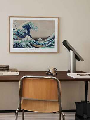 Inramad Hokusai-vågposter ovanför träskrivbord med lampa, kopp, böcker och stol