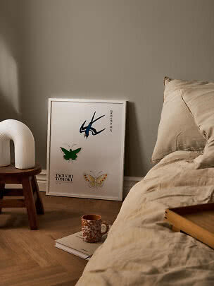 Camera da letto con biancheria beige, sgabello in legno con lampada bianca e poster incorniciato