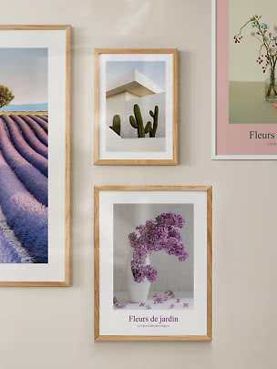 Bilderwand mit hellen Holzrahmen und Drucken von Lavendelfeld, Kakteen und lila Blumen