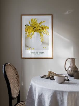 Framed floral print with yellow mimosa in a white vase above a table setting