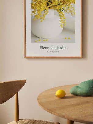Framed floral poster above a wooden table with a lemon and green sculptural object