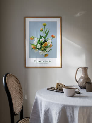 Ingelijste bloemenposter met tulpen boven een tafel met kopje, cake en keramische vaas