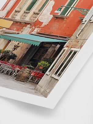 Foto inclinada de una fachada de café con pared naranja, persianas verdes y mesas exteriores