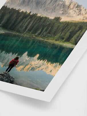 Persona con zaino presso un lago di montagna con bosco e rocce riflesse nell’acqua