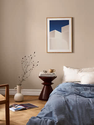 Bedroom with blue bedding, dark side table, vase, and framed artwork on a beige wall