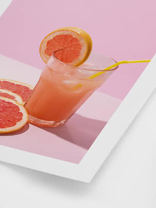 Glas med pink grapefrugtdrik, isterninger, gult sugerør og grapefrugtskive på lyserød baggrund