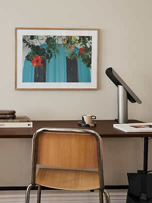 Home office with wooden desk, chair, lamp, and framed floral print on the wall