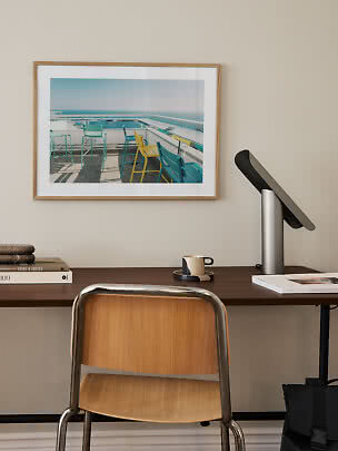 Framed art print above desk with chair, lamp and cup in a minimalist home office