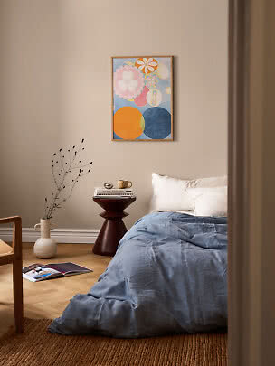 Camera da letto con biancheria blu, cuscini bianchi, tavolino rotondo e quadro astratto colorato
