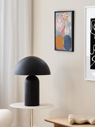 Lampada da tavolo nera con paralume a cupola su tavolino bianco in una stanza luminosa