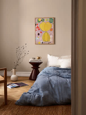 Camera da letto con biancheria blu, cuscini bianchi, tavolino e quadro astratto colorato a parete