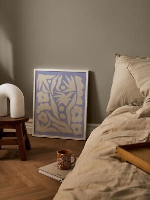 Bedroom with beige bedding, stool with white lamp, and purple floral poster on the floor