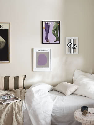 Slaapkamer met witte kussens en dekbedden en drie ingelijste posters aan een beige muur