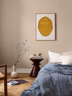 Camera da letto con letto, tavolino e poster incorniciato con volto giallo su parete beige