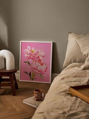 Framed poster of pink flowers on a pink background beside a bed in a bedroom