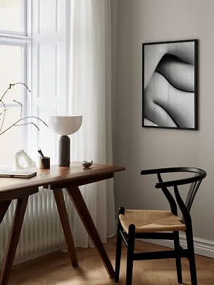 Black framed abstract poster on beige wall above desk and black chair