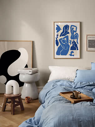 Cozy bedroom with light blue bedding, wooden tray, mug, and abstract framed wall art