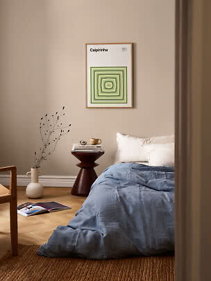 Framed poster with green geometric design above a bed in a beige bedroom