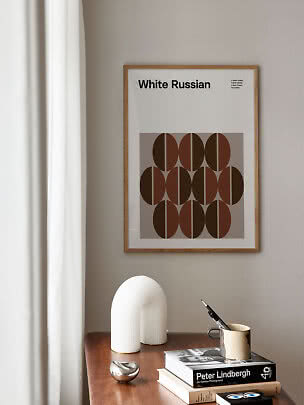 Ingelijste White Russian-poster boven een houten tafel met boeken, vaas en mok