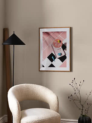 Indrammet lyserødt kunstprint på beige væg over hvid lænestol i moderne stue