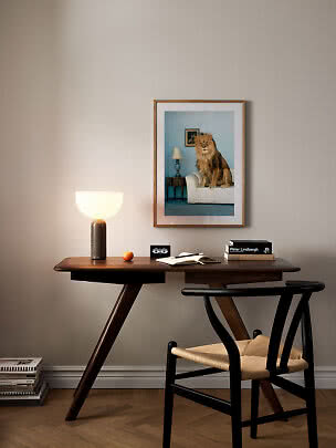 Skrivbord i trä med bordslampa, bok och stol under en inramad lejonbild på väggen