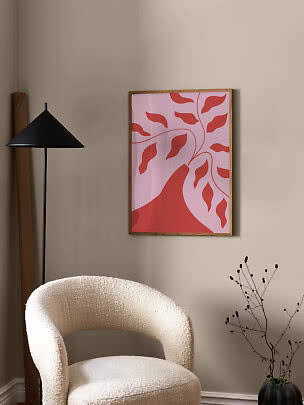 Póster abstracto enmarcado con hojas rojas sobre fondo rosa encima de una silla color crema
