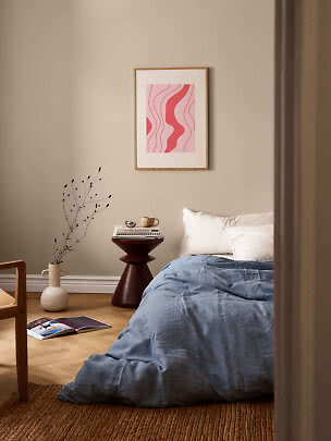 Gerahmter abstrakter rosa Wellenprint über einem Bett in einem gemütlichen Schlafzimmer
