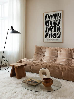 Modern living room with beige sofa, black floor lamp, glass table and abstract wall poster