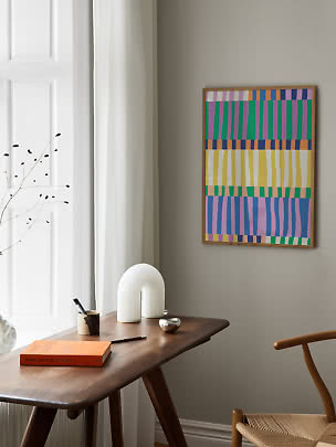 Colorful abstract art print in a wooden frame above a wooden desk by the window