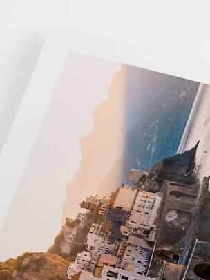 Printed photo with white border of a coastal town at sunset, with cliffs, buildings and sea