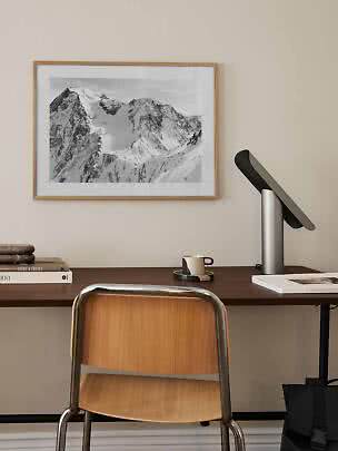 Gerahmtes Schwarz-Weiß-Bergbild über einem Schreibtisch mit Stuhl, Lampe, Büchern und Tasse