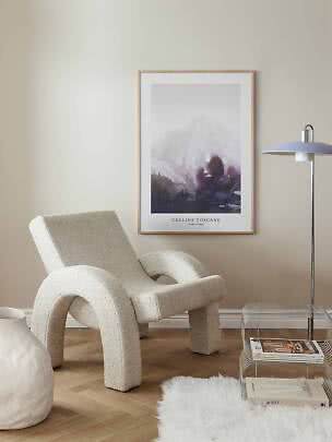 Poster of a misty mountain landscape in a light wood frame above a cream lounge chair.