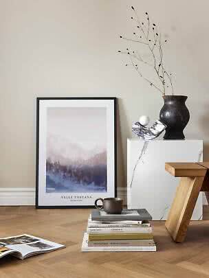 Gerahmtes Valle-Toscana-Poster an der Wand mit Vase, Büchern und Tasse auf Holzboden