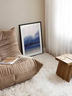 Cozy corner with beige lounge chair, blue abstract art print, small wooden table and white rug