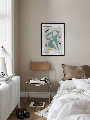 Bedroom corner with framed abstract poster above chair, bed, lamp and books