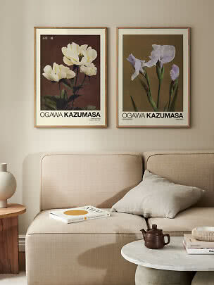 Two framed botanical flower posters hang above a beige sofa in a calm living room.