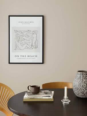 Framed art poster with sketch of nude figures in a beach scene above a dark table