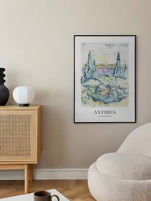 Framed Antibes landscape art print hanging above a wooden cabinet in a living room