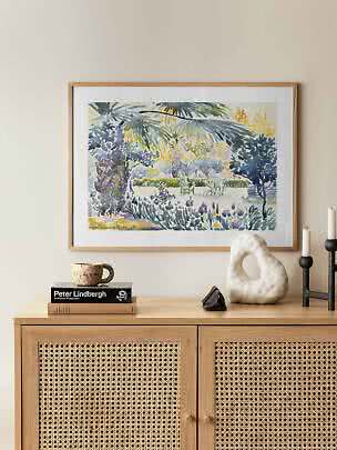 Gerahmtes Aquarell mit Palmen und Gartenszene über einem hellen Holzschrank mit Dekoobjekten.