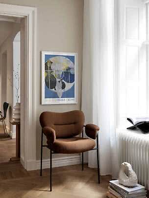 Brauner Polsterstuhl mit schwarzem Gestell am Fenster und abstraktem Poster an beigefarbener Wand