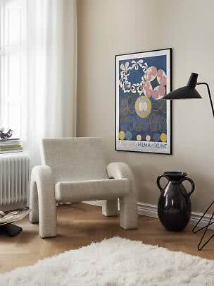 Coin cosy avec fauteuil crème, lampadaire noir et affiche encadrée de Hilma af Klint sur mur beige