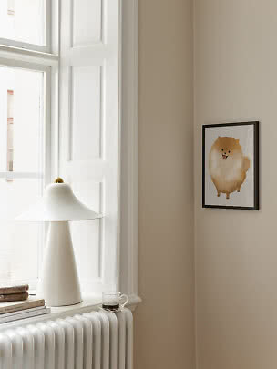 Poster incorniciato con tenero cane soffice su parete beige accanto a finestra e lampada bianca