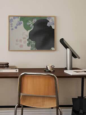 Desk with wooden chair, table lamp and framed floral print on a light wall
