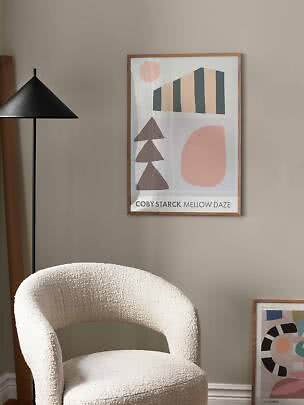 Poster astratto incorniciato su parete beige sopra una poltrona color crema accanto a una lampada nera